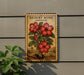 A decorative sign featuring a desert rose plant with red flowers is mounted on a wall, accompanied by a potted plant to the left.