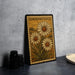 A vintage-style metal stamp with a floral design, featuring three large white daisies, is displayed on a dark surface next to a stack of black camera lenses.