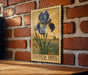 A 50 cent Dutch postage stamp featuring an illustration of a blue iris flower is displayed on a brick wall.