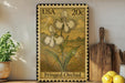 A framed image of two white orchid flowers on a wooden shelf, with a wooden cutting board and a potted plant to the left.