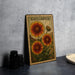 A metal sign with a vintage-style illustration of three sunflowers and the word "GAILLARDIA" on it, placed on a gray countertop next to some black camera lenses.