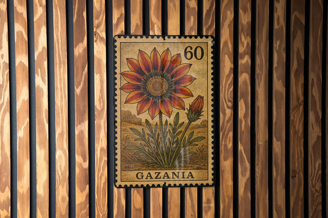 A postage stamp from Gazania, featuring a large flower with a red center and yellow petals, is displayed on a wooden wall.