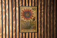 A postage stamp from Gazania, featuring a large flower with a red center and yellow petals, is displayed on a wooden wall.