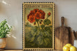 A framed illustration of a geranium plant with a wooden cutting board and lemons in the foreground, placed on a shelf against a white wall.