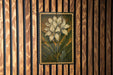 a framed painting of a white flower on a wooden wall.
