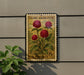 A U.S. postage stamp featuring a vibrant red flower on a green background, mounted on a wall next to a plant.
