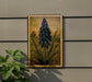 a framed painting of a blue flower on a wall, with a plant next to it.