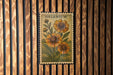 A vintage-style postage stamp featuring a floral design with three sunflowers is displayed on a wooden wall.