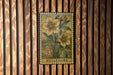 A metal stamp with a floral design is hanging on a wooden wall.
