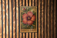 A framed illustration of a red hibiscus flower is displayed on a wooden wall.