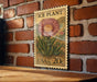 A vintage-style postage stamp featuring a large pink flower is displayed on a brick wall.
