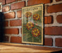 A framed vintage postage stamp depicting a vibrant floral scene is displayed on a brick wall.