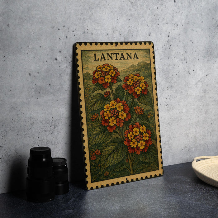 A framed print of a floral illustration with the word "LANTANA" on it, placed on a table next to some black camera lenses.