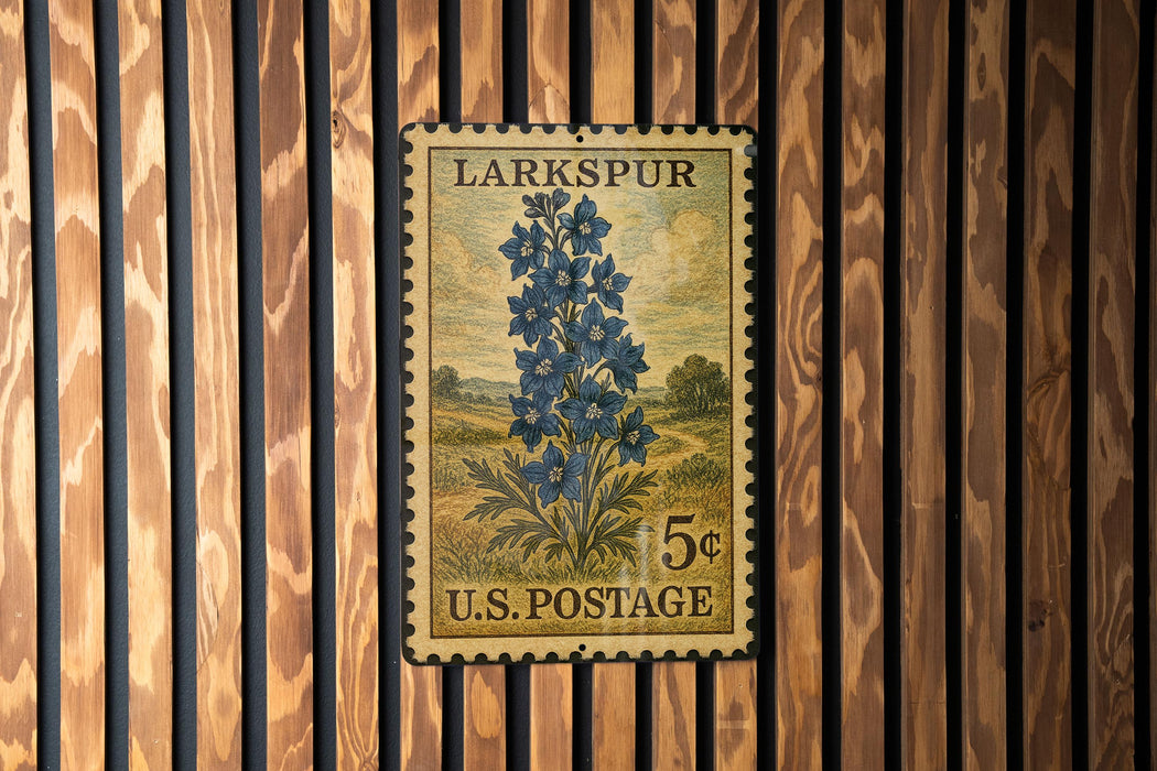 A vintage U.S. postage stamp from Larkspur, featuring a blue flower illustration, is displayed on a wooden wall.