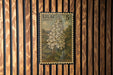 A vintage postage stamp featuring a detailed illustration of a white lilac flower, mounted on a wooden wall.