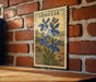 A vintage postage stamp featuring a blue flower is displayed on a brick wall.