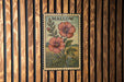A framed vintage stamp depicting two red hibiscus flowers is displayed on a wooden wall.