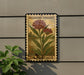 A vintage-style postage stamp featuring a milkweeds swamp plant, mounted on a wall next to a plant.