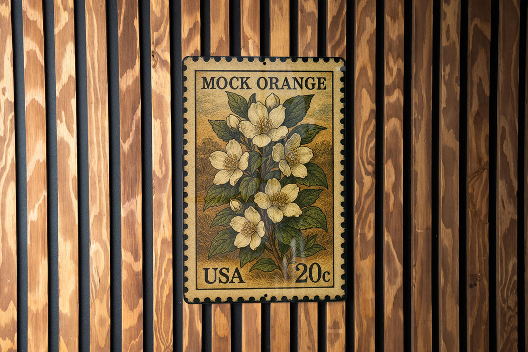 A vintage-style postage stamp from the United States, featuring a floral design with white flowers and green leaves, mounted on a wooden wall.
