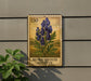 a postage stamp-like sign with a depiction of blue flowers, mounted on a wall next to a plant.