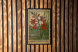 A framed postcard with a floral illustration is hanging on a wooden wall.