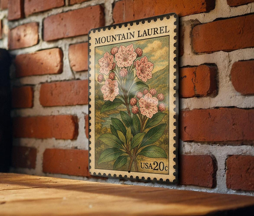 A vintage-style postage stamp featuring a floral illustration of a mountain laurel plant, mounted on a brick wall.