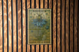 A vintage postage stamp featuring a blue flower is displayed on a wooden wall.