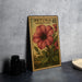 A metal stamp with a floral design, featuring a large red flower surrounded by green leaves, is displayed on a table.