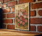 A vintage-style stamp featuring a floral illustration is displayed on a brick wall, with a wooden table below it.