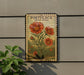 A vintage-style metal sign with a floral illustration of red flowers, mounted on a wall next to a plant.