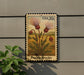 A postage stamp featuring a floral illustration of a plant with red flowers, mounted on a wall next to a plant.