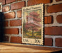 A wooden table with a framed stamp depicting a tree with pink flowers, mounted on a brick wall.