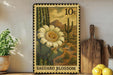 A decorative metal stamp featuring a cactus flower and a desert landscape, with the text "Saguaro Blossom" printed on it. The stamp is placed on a shelf next to a wooden cutting board and a potted plant.