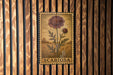 a floral stamp with the word "SCABIOSA" printed on it, which is displayed on a wooden wall.