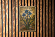 a framed illustration of blue flowers on a wooden wall.