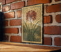 a decorative metal frame with a vibrant red flower and green leaves, mounted on a brick wall.