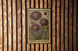 A framed illustration of a flower is hanging on a wooden wall.