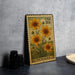 A metal stamp featuring a yellow flower design with the word "TICKSEED" printed on it, placed on a gray countertop next to some black camera lenses.