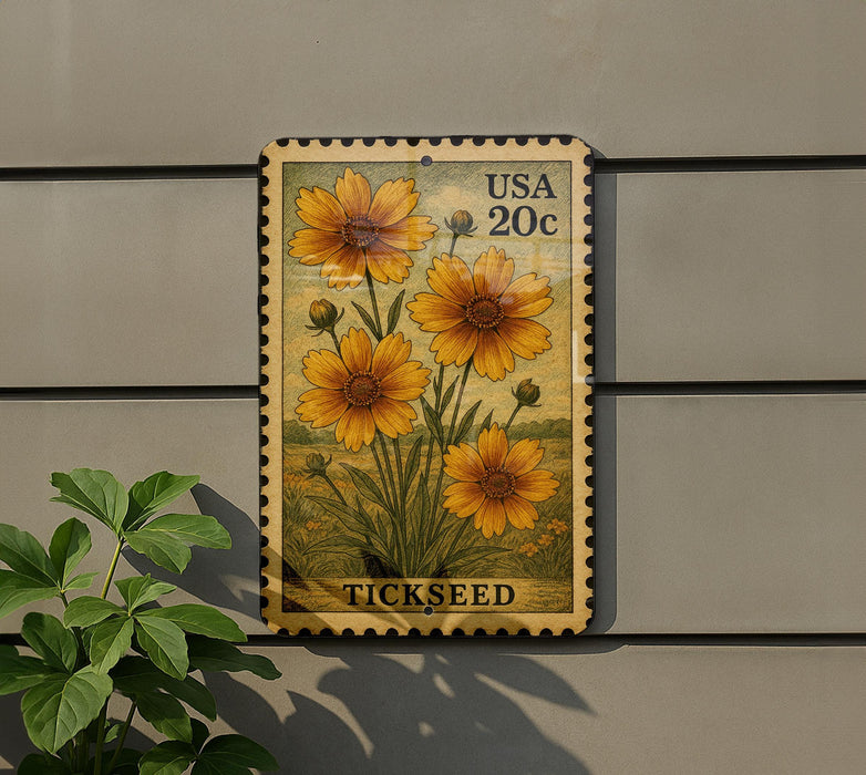 A postage stamp featuring a vibrant illustration of yellow flowers, with the word "TICKSEED" printed below. The stamp is affixed to a gray wall, and there is a small green plant to the left of the stamp.