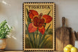 A framed illustration of a large red flower with yellow spots, surrounded by green leaves, is displayed on a shelf next to a wooden cutting board and a potted plant.