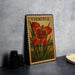 A framed illustration of a large red flower with green leaves, labeled "TIGRIDIA", is displayed on a gray wall.