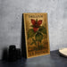 A framed stamp depicting a red flower with green leaves, placed on a table next to a stack of black camera lenses.