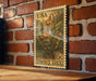 A wooden table with a brick wall in the background, featuring a framed US postage stamp depicting a lily flower.