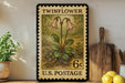A vintage-style postage stamp featuring a floral illustration, placed on a wooden surface next to a wooden cutting board and some potted plants.