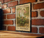 A vintage-style postage stamp featuring a pink flower on a brick wall.