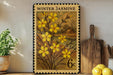 A framed print of a yellow flower design is displayed on a shelf, surrounded by kitchen utensils and a potted plant.