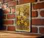A vintage-style postage stamp featuring a floral design with yellow flowers, mounted on a brick wall.
