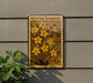 A vintage-style postage stamp featuring a floral design with yellow flowers, mounted on a wall next to a plant.