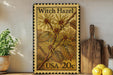 A metal stamp with a floral design and text, placed on a shelf next to a wooden cutting board and a potted plant.
