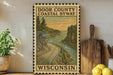 a framed vintage-style poster of Door County, Wisconsin, with a scenic coastal highway and landscape. The poster is displayed on a shelf next to a wooden cutting board and a potted plant.